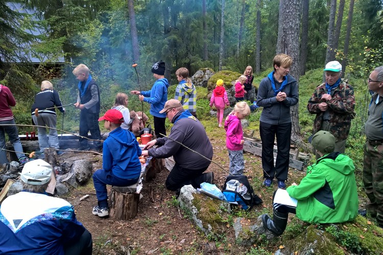Seurakunnan lapsityön toimintaa: perhevaelluksella perheitä metsässä tauolla paistamassa makkaraa